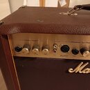 Detail ovládacího panelu hnědého komba značky Marshall. Zlatý kovový panel obsahuje nápisy Acoustic Channel 1 a Microphone / Aux Channel 2 s odpovída…