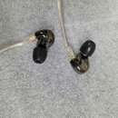 Dva černý in-ear monitory s průhledným kabelem. Na obou sluchátkách je viditelný nápis SE846 a symbol registrované ochranné známky. Povrch sluchátek…