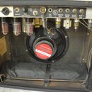 Interiér kytarového komba s viditelným šasi, elektronickými komponenty a reproduktorem. Na horní kovové liště jsou nápisy FENDER MUSICAL INSTRUMENTS…
