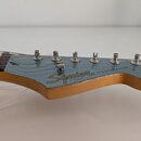 Fotografie zachicuje hlavu elektrické kytary v modré barvě s viditelnou dřevěnou hranou. Na povrchu je nápis Squier BY FENDER a STRATOCASTER®. Jsou v…