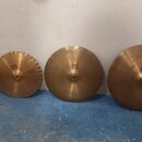 Šest mosazných činelů opřených o bílou zeď na modré podlaze. Na čtyřech středových činelech je vidět logo Paiste a nápis 2002. Povrchy činelů vykazuj…