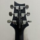 Zadní strana hlavy černé kytary s chromovanými ladičkami. Na zadní straně hlavy je bílý nápis: Built by Cor-Tek Musical Instrument Co., LTD, Indonesi…