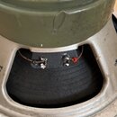 Fotografie zachicuje zadní stranu reproduktoru s olivově zeleným magnetem a stříbrným rámem. Na horní části magnetu je černé kulaté logo s nápisy MAD…