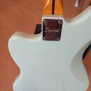 Zadní strana elektrické kytary v bílé barvě s dřevěným hřednicí. Na kovovém spojovacím pláštěm mezi tělem a hřednicí je vyryto logo Squier. Povrch la…