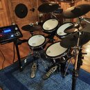 Elektronická bicí souprava značky Roland s černými pady a činely. Součástí je ovládací modul s nápisem Roland a několika tlačítky a displejem. Všechn…