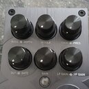 Kovové ovládací panel s broušeným povrchem a šesti černými otočnými knoflíky. Pod knoflíky jsou nápisy BASS-C DEPTH, MIDDLE, TREB-C PRES, OUT-C GATE,…