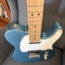 Modrá elektrická kytara typu Telecaster s bílým pickguardem a hnedým javorovým hmatníkem. Na těle je vidět jeden snímač a kovový most s saddles. Povr…