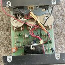 Fotografie zachycuje vnitřek elektronického zařízení s otevřeným šasi. Je vidět zelená základní deska s osazenými součástkami, transformátor a dva ve…