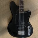 Černá elektrická basová kytara s tmavým hnedým hmatníkem. Nástroj má černý pickguard a chromovaný most s integrovaným pákovým systémem. Na těle nejso…