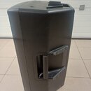 Černý plastový reproduktor s hranatým tvarem a zaoblenými hranami. Na boku je umístěna integrovaná rukojeť s protiskluzovými gumovými vložkami. Na ho…
