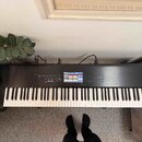 Černý klavír s bílými a černými klávesami. Na levé straně je nápis KORG a na pravé straně nápis NAUTILUS MUSIC WORKSTATION. V horní části se nachází…