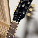 Černá hlava kytary s bílým logem Gibson. Na čele je umístěn stříbrný ornament ve tvaru koruny a bílé ladičky. Na povrchu hlavy je viditelný bílý obry…
