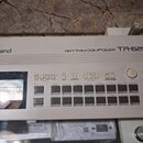 Bílý rytmický kompozér Roland RHYTHM COMPOSER TR-626. Zařízení obsahuje displej s mřížkou, několik řad ovládacích tlačítek a dva otočné ovladače ozna…