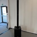 Černý sloukový reproduktor s subwooferem v základně. Na horní části sloupce i na spodní části subwooferu je viditelné logo JBL. Povrch je matný a v d…
