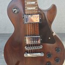 Hnědá elektrická kytara s tmelem a dvěma humbuckery. Na přepínači je nápis TREBLE a RHYTHM. Kytara má čtyři ovládací knoflíky, chromovaný most a stop…