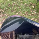 Detailní pohled na tělo elektrické kytary v tmavě fialové barvě s lesklým povrchem. Na instrumentu je vidět černý humbuker a černý most s nápisem Flo…