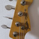 Záběr na hlavu basové kytary z přírodního dřeva s kovovými ladicími kolíky. Na zadní straně je vidět logo Fender a nápis JAZZ BASS MADE IN USA ELECTR…