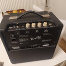 Černý basový kombo zesilovač s nápisem Rumble 75. Na horním ovládacím panelu jsou čtyři bílé otočné knoflíky s popisky TREBLE, MID, BASS a VOLUME, vs…