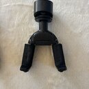 Černý držák na nástroj s dvěm polstrovanými rameny. Předmět je vyroben z kovu a syntetického materiálu, povrch je matný. Na fotce nejsou viditelné žá…