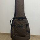 Hnědý polstrovatý pouzdro na kytaru s černými zipy a úchyty. Na přední kapse je vyveden velký nápis SE a pod ním logo PRS GUITARS s doplňkem SE. Povr…