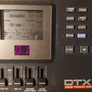 Černý elektronický modul s displejem a ovládacími prvky. Na spodní části je bílý nápis DTX Version 2.0 a pod ním červený pruh s textem DRUM TRIGGER M…