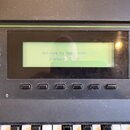 Detailní záběr na ovládací panel klaviatury s displejem. Na displeji je text: Welcome to the K2000! (Version 2.08J). Vlevo jsou tlačítka s nápisy CHA…