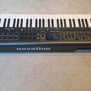 Černý MIDI kontrolér s klaviatura a červenými bočními panely. Na přední straně je bílý nápis novation a vlevo označení IMPULSE. Ovládací panel obsahu…