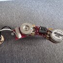 Elektronika pro kytaru s dvěma snímači a potenciometrem na červené desce plošných spojů. Pravý snímač má na krytu nápis OBSIDIAN Wire QUALITY GUARANT…