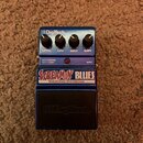 Modrý kytarový efekt s nápisy SCREAMIN' BLUES a OVERDRIVE/DISTORTION. Na pravé straně jsou čtyři ovládací knoflíky s popisky LEVEL, LOW, HIGH a GAIN…