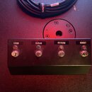 Černý obdélníkový spínací box s четыma kovovými tlačítky. Nad každým tlačítkem je nápis: LEAD, CLEAN, REVERB a BOOST. Nad tlačítky jsou umístěny kont…
