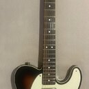 Elektrická kytara s tónem sunburst a bílým pickguardem. Na hlavě hředu je viditelné logo Squier by Fender a nápis CUSTOM TELECASTER. Nástroj je v dob…