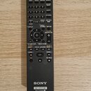 Černý dálkový ovladač značky SONY s nápisem AV SYSTEM a označením RM-AAU020 R. Obsahuje početnou sadu tlačítek pro ovládání různých funkcí, včetně nu…