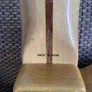 Záběr na zadní stranu krku kytary z jasného dřeva s tmavým středovým pruhem. U základny krku je černý nápis MADE IN JAPAN. V dolní části je vidět kov…