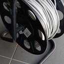 Černý plastový kabelový navíjač s rukojetí, na kterém je namotaný šedý kabel. Na boku navíjače je viditelná bílá nálepka s nápisem BV4. Povrch plastu…