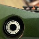 Detailní záběr na zelený lakovaný povrch nástroje s kovovým zapojovacím konektorem. Kolem otvoru pro konektor je vidět opotřebení laku a odlouštění p…