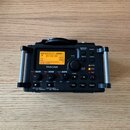 Černý digitální záznamový přístroj značky TASCAM s LCD displejem, na kterém je vidět nápis NO CARD. Zařízení má ovládací tlačítka DATA, MENU, QUICK a…