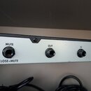 Detail zadní strany bílého elektronického zařízení s černým horním okrajem. Jsou zde tři konektory s nápisy MUTE (pod kterým je text CLOSE=MUTE), OUT…