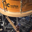 Dřevěný buben v přírodní světle hnědé barvě s nápisem Custom made USA a grafickým motivem křídel. Buben je umístěn na chromovaném stojanu, ve kterém…