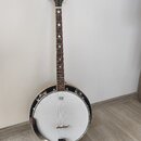 Banjo s bílou membránou a hnědým hředníkem. Na hlavě nástroje je logo SX, na membráně je viditelný nápis Washburn. Hředník má v inlaidových polích bí…
