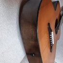 Akustická kytara s hnědým povrchem a tmavými boky. Na těle je vidět černý plechtráček a hnedopřírodní barva desky. Povrch vykazuje drobné známky opot…