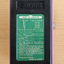 Zadní strana fialového efektpedálu s černým kovovým krytem. Na krytu je vyražené logo BOSS a nalepený zelený štítek s nápisem BOSS AC ADAPTOR, který…