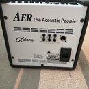 Zadní strana bílého komba s černým rámem. Na horní části je nápis AER The Acoustic People®, níže označení Alpha. Jsou zde viditelné konektory pro hea…