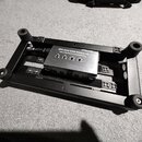 Černý kovový pedalboard s gumovými nožičkami, na kterém je umístěn napájecí zdroj. Na zdroji je nápis ISO-3AC SAG MODULAR ISOLATED OUTPUT POWERPLANT…
