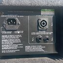 Fotografie zachycuje zadní panel elektronického zařízení s černým povrchem. Na panelu jsou umístěny napájecí konektor, jeden výstup označený jako SPE…