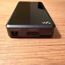 Černý přenosný digitální přehrávač s kovovým povrchem. Na spodní hraně jsou vidět nápisy NW-WM1A a 5003164, USB port a slot pro kartu. Na horní části…