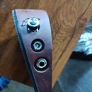 Hnědý kožený popruh s integrovaným elektronickým prvkem. Jsou na něm vidět regulační knoflík, vstup pro napájení s nápisem DC 9V a výstupní jack s ná…