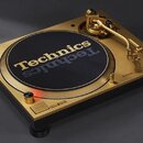 Zlatý gramofon s černým talířem, na kterém je bílý nápis Technics. Na šasi je viditelné logo Technics a tlačítko s nápisem START-STOP. Nástroj vykazu…