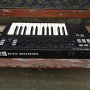 Černý MIDI kontrolér s klaviaturní klávesou. Na zadní straně je bílý nápis NATIVE INSTRUMENTS a logo NI, vpravo nahoře je text KOMPLETE KONTROL S25.…