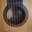 Detail akustické kytary s viditelným otvorem rezonanční skříně a částí hmatníku. Uvnitř otvoru je štítek s nápisem SCHNIDER GUITAR a CZESKOSLOVAKIA,…