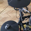 Elektronická bicí souprava s dvěma černými gumovými činely značky Roland. Činely jsou upevněny na kovovém stojanu a jsou připojeny kabely. V dolní čá…